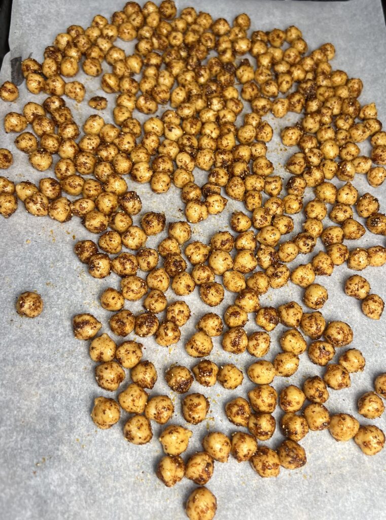 A close-up image of chickpeas coated in a vibrant blend of spices, including chili powder, smoked paprika, and cumin, glistening with olive oil as they sit evenly spread on a parchment-lined baking sheet, ready to be baked to crispy perfection.