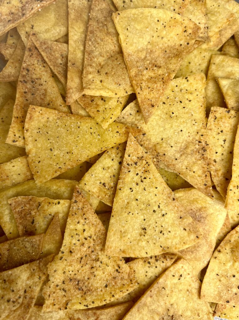 A close-up of golden, crispy oven-baked tortilla chips, perfectly toasted with lightly browned edges, showcasing their crunchy texture.