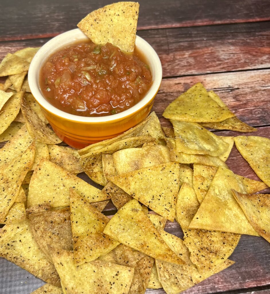 A close-up image of golden, crispy oven-baked tortilla chips arranged on a platter, paired with a vibrant red bowl of fresh salsa, garnished with cilantro.