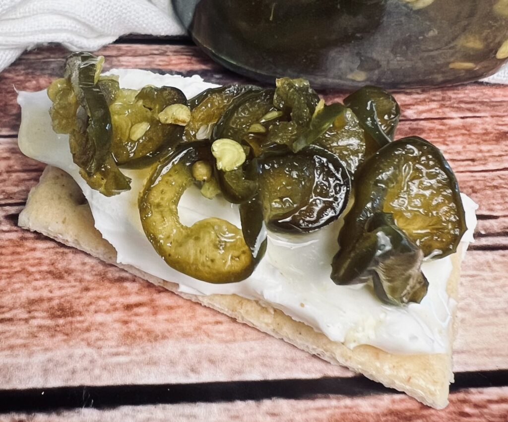 Cracker topped with cream cheese and sweet, spicy candied jalapeños, showcasing a delicious appetizer idea