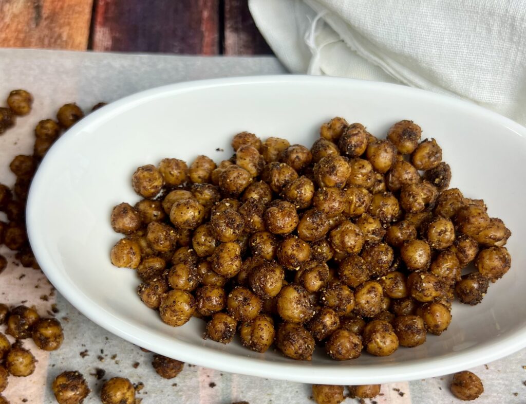 Golden-brown roasted chickpeas in a bowl, surrounded by scattered crispy chickpeas on parchment paper, showcasing their crunchy texture and rich Southwest seasoning.