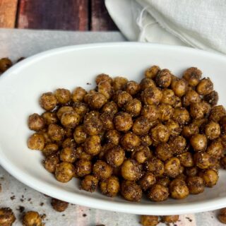 Golden-brown roasted chickpeas in a bowl, surrounded by scattered crispy chickpeas on parchment paper, showcasing their crunchy texture and rich Southwest seasoning.